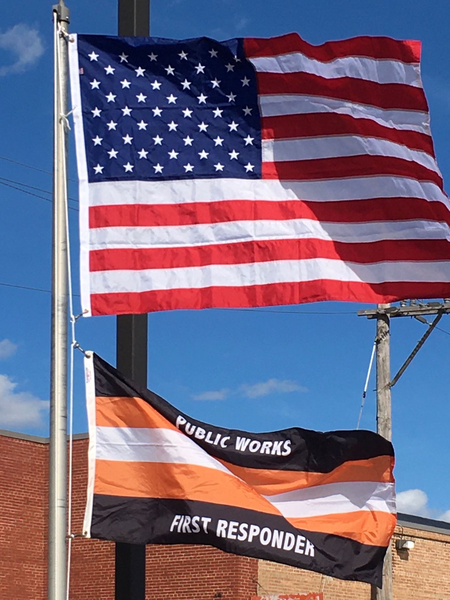 Red, white and blue American flag flying above a white, black and orange public responder flag.